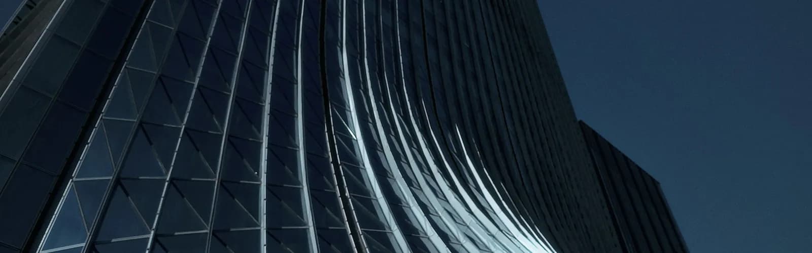 Curved glass tower facade illuminated at night